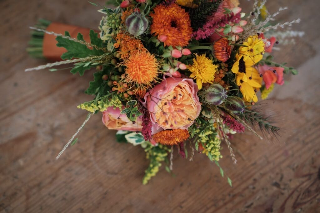 Hochzeitskrone Ein bunter Strauß mit Rosen, Ringelblumen, Mohn und Grünzeug liegt auf einer Holzoberfläche – die perfekte Ergänzung, um echte Momente eines Hochzeitsfotografen in Wien und Niederösterreich festzuhalten.