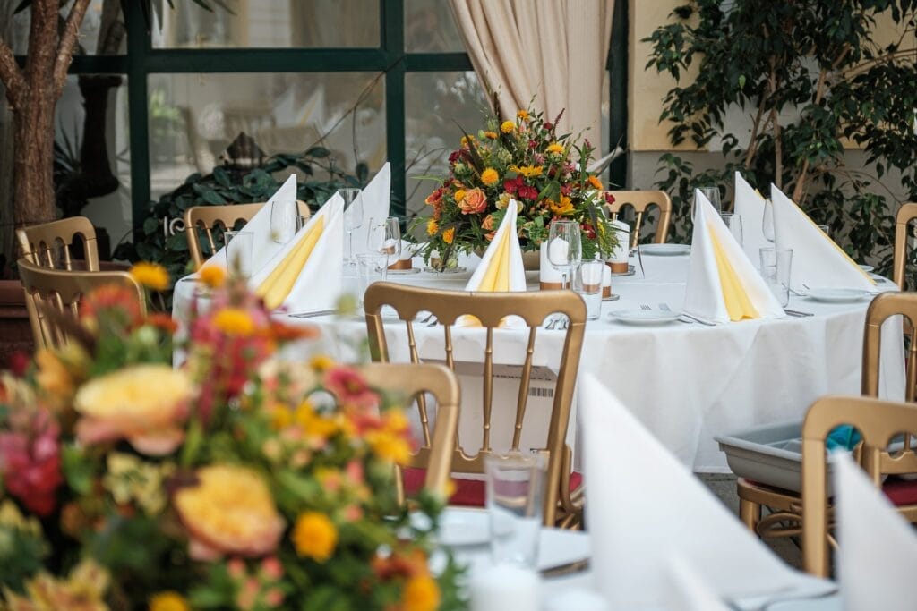 Hochzeitskrone Für eine formelle Veranstaltung gedeckte Tische mit weißen Tischdecken, gefalteten Servietten, Glaswaren und farbenfrohen Blumengestecken erinnern an die Eleganz, die oft in authentischen Hochzeitsfotos eingefangen wird.