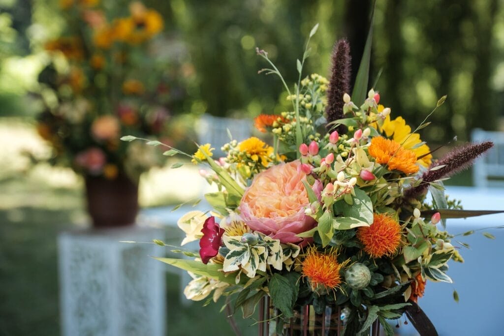 Hochzeitskrone Ein farbenfroher Strauß mit gelben Sonnenblumen, rosa Rosen, orangefarbenen und roten Blumen und üppigem Grün fängt im Freien bei natürlichem Licht echte Momente ein.