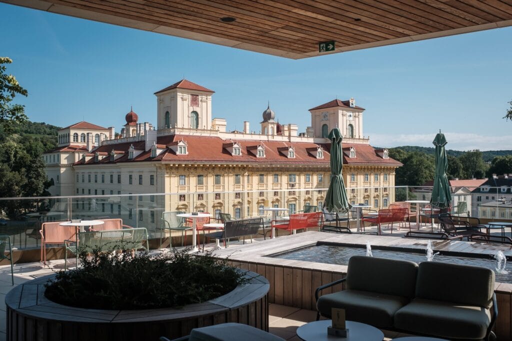 Hochzeitskrone Von der Dachterrasse mit Sitzgelegenheiten haben Sie einen Blick auf ein historisches Gebäude, dessen rote Dächer und Türme einen schönen Kontrast zum klaren blauen Himmel bilden – perfekt für natürliche Hochzeitsfotos.