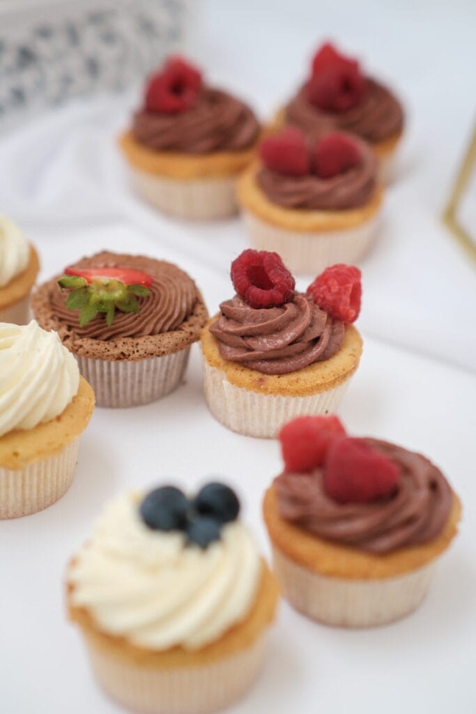 Hochzeitskrone Genießen Sie eine köstliche Auswahl an Cupcakes mit authentischen Toppings, wie Schokoladenglasur mit Himbeeren, Vanilleglasur mit Blaubeeren und Schokoladenglasur mit einer geschnittenen Erdbeere obendrauf. Halten Sie diese süßen Momente fest, so wie ein Hochzeitsfotograf in Wien und Niederösterreich echte Hochzeitserinnerungen festhält.