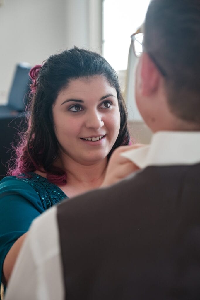 Hochzeitskrone Eine Frau in Blau richtet zärtlich den Kragen eines Mannes im Haus und fängt damit einen jener bezaubernden Momente ein, die man oft auf natürlichen Hochzeitsfotos findet.