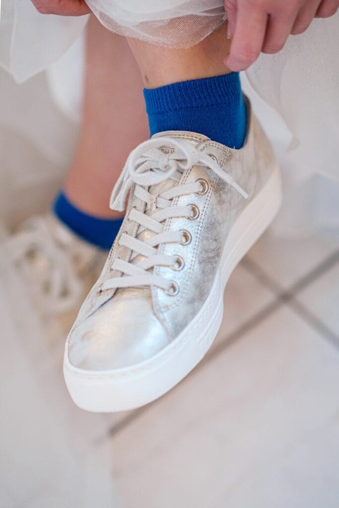 Hochzeitskrone Eine Person schnürt einen silbernen Sneaker und kombiniert ihn mit blauen Socken und fängt damit einen jener bezaubernden Momente ein, die natürliche Hochzeitsfotos oft offenbaren.