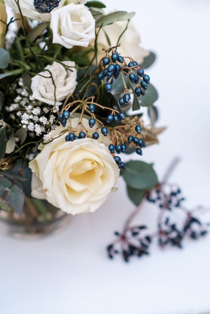 Hochzeitskrone Ein Strauß mit weißen Rosen, kleinen weißen Blüten und Trauben dunkler Beeren, arrangiert mit grünem Laub auf weißem Hintergrund, fängt bezaubernde Momente ein, perfekt für natürliche Hochzeitsfotos.