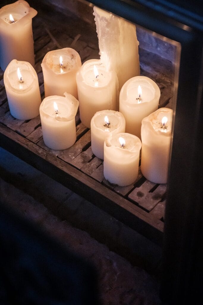 Hochzeitskrone Eine Sammlung brennender weißer Kerzen unterschiedlicher Höhe, angeordnet auf einem Holzgitter, fängt bezaubernde Momente ein und erinnert an den Charme natürlicher Hochzeitsfotos.