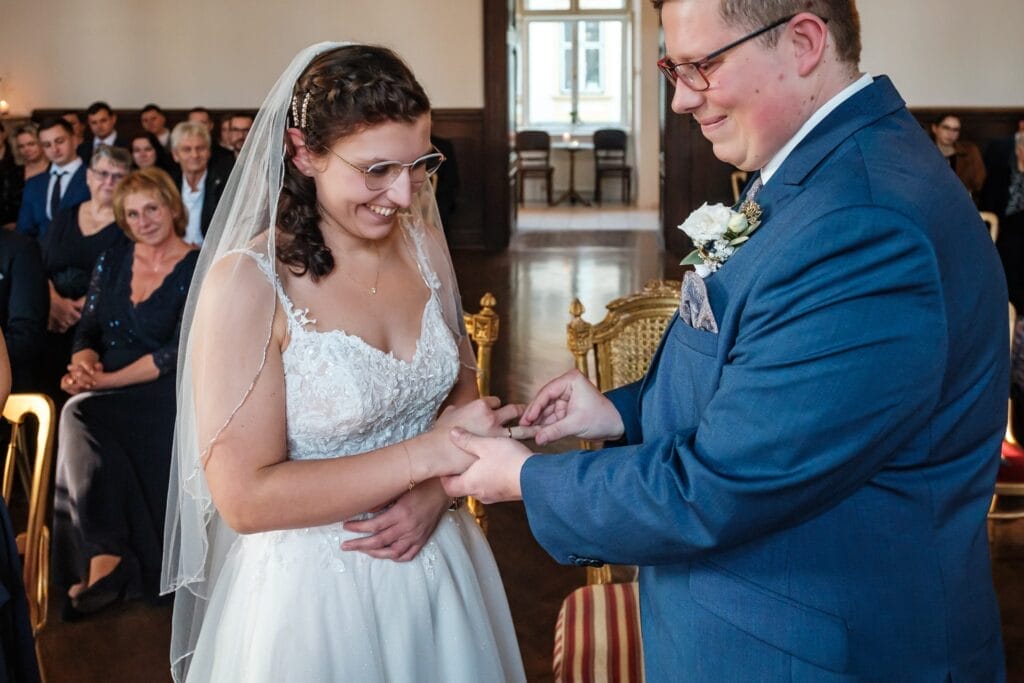 Hochzeitskrone Braut und Bräutigam tauschen in einer magischen Zeremonie Ringe aus, festgehalten durch natürliche Hochzeitsfotos, umgeben von sitzenden Gästen. Diese bezaubernden Momente der Liebe und Hingabe strahlen in jedem Bild der Hochzeitsfotografie in Niederösterreich.