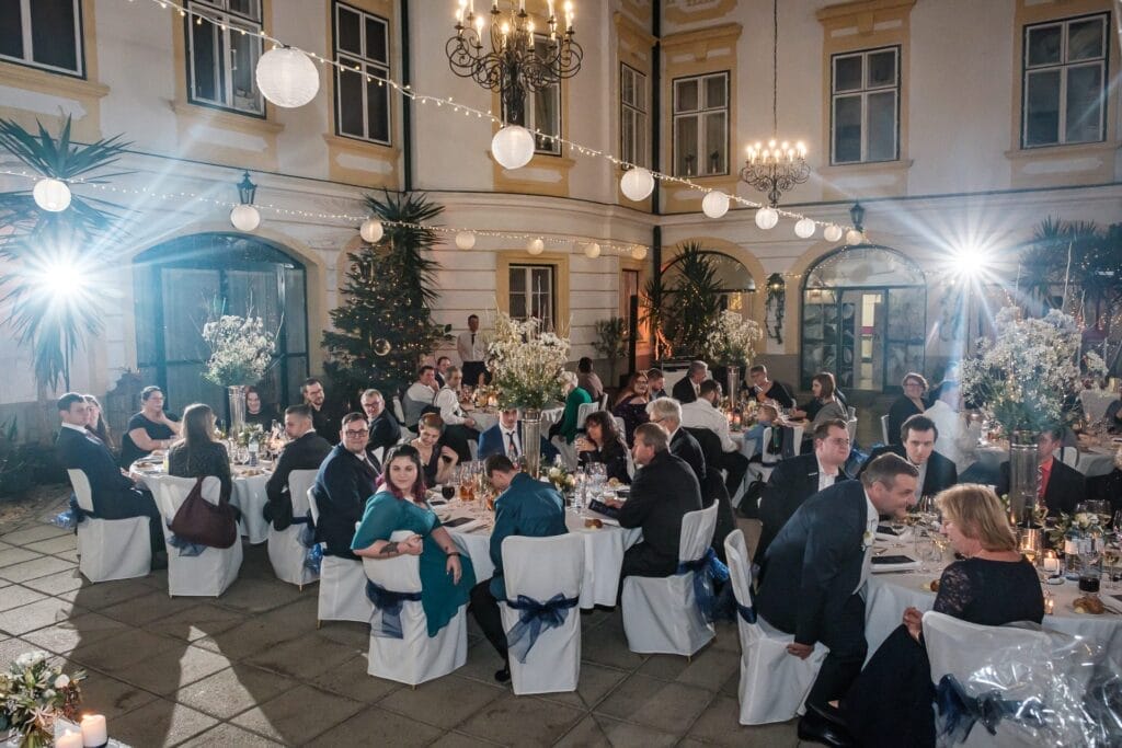 Hochzeitskrone Gäste sitzen an dekorierten Tischen in einem Innenhof mit Lichterketten und Kronleuchtern und fangen bezaubernde Momente ein, perfekt für natürliche Hochzeitsfotos.