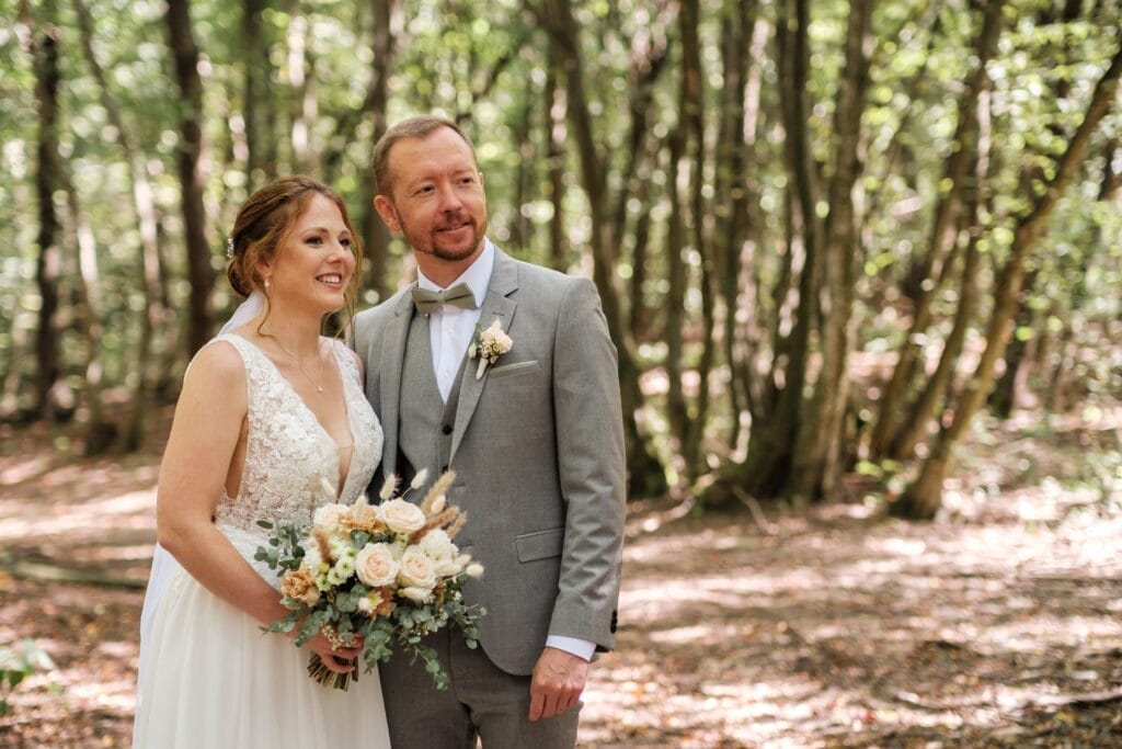 Hochzeitskrone Ein Paar im Hochzeitskleid steht in einem Wald und fängt bezaubernde Momente ein. Die Braut hält einen Blumenstrauß in der Hand, ihr Lächeln spiegelt die Essenz natürlicher Hochzeitsfotos wider.