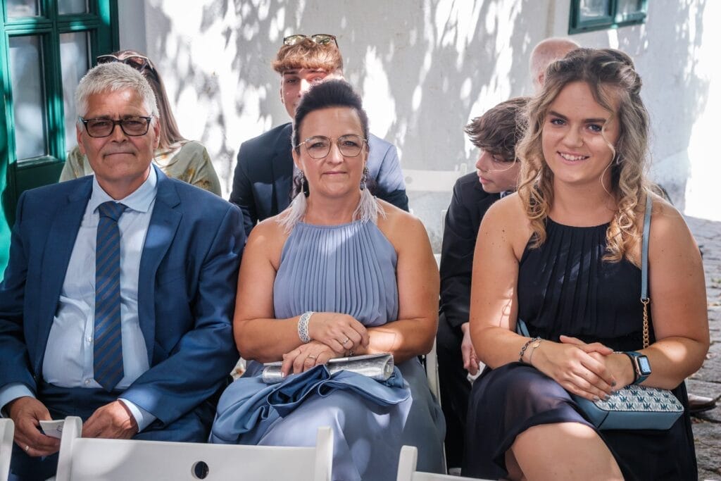 Hochzeitskrone Drei Personen, elegant in Abendgarderobe gekleidet, sitzen inmitten der zauberhaften Natur, während die Bäume komplexe Schatten werfen – und fangen bezaubernde Momente ein, ideal für Hochzeitsfotografie in Niederösterreich.