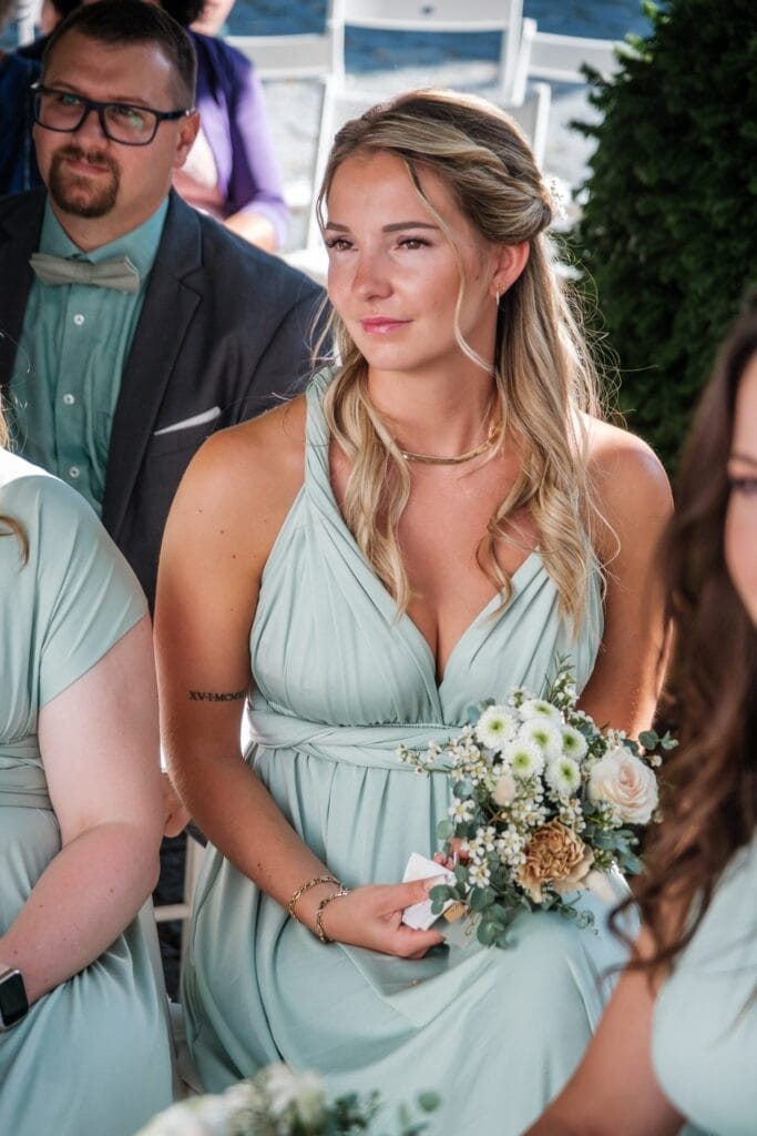 Hochzeitskrone Eine Frau in einem hellgrünen Kleid hält einen Blumenstrauß in der Hand, während sie im Freien sitzt, umgeben von anderen in ähnlicher Kleidung. Es ist eine Szene bezaubernder Momente, festgehalten durch natürliche Hochzeitsfotos, die die Essenz der Hochzeitsfotografie in Niederösterreich hervorhebt.