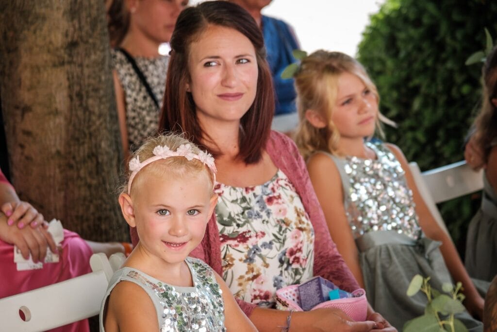 Hochzeitskrone Eine Frau und zwei Kinder sitzen zusammen im Freien und fangen bezaubernde Momente ein. Die Frau trägt ein geblümtes Kleid, während die Kinder in funkelnden silbernen Outfits glänzen. Perfekt für natürliche Hochzeitsfotos in Niederösterreich, strahlt diese Szene Wärme und Freude aus.