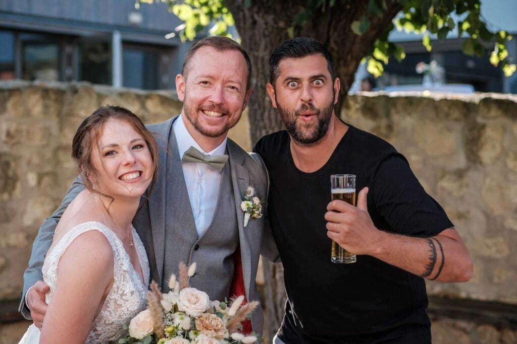 Hochzeitskrone Das Brautpaar lächelt und fängt bezaubernde Momente mit einem Mann ein, der ein Bier unter dem Baum hält und natürliche Hochzeitsfotos präsentiert.